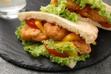 Delicious pita sandwiches with fried fish, pepper, tomatoes and lettuce on dark grey table, closeup