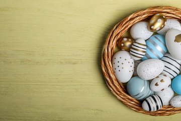 Decorative nest and many beautiful Easter eggs on yellow wooden table, top view. Space for text