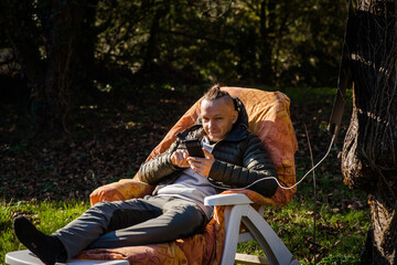 Fototapeta na wymiar A portable solar battery is hanging from a tree. A man resting in nature with a mobile phone in his hands. Charging phone from solar eco energy.