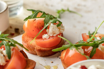 Bruschetta with tomatoes, arugula, olive oil and cheese on white tray on textured background close up. Fresh italian toasts