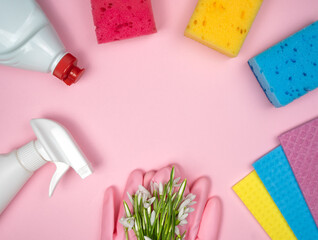 Detergent and cleaning products, kitchen sponges, rubber gloves lie in the shape of a frame on a pink background. Spring cleaning. Top view. Flatlay. Copy space.