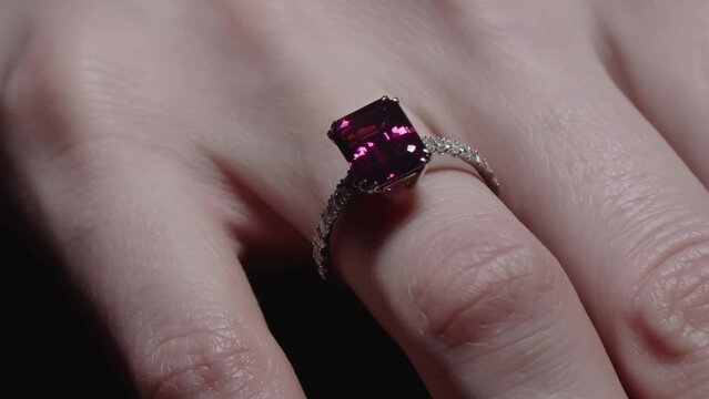 Red ruby diamond engagement ring on woman's finger. Light sweeping over the hand.