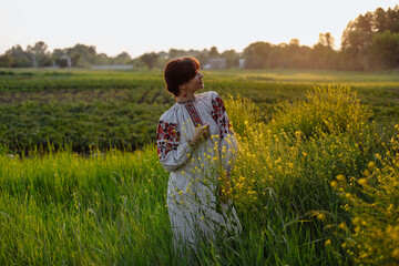 A girl in a national costume in a field against a background of green bushes and trees