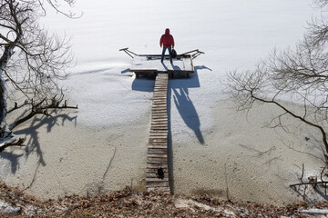 Sunny frosty winter day. Ice on a river or lake. Tourist or traveler with a backpack in his hand. Wooden bridge for fishing