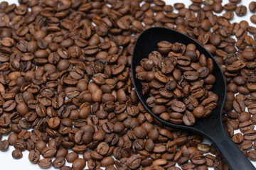 Rozsypane ziarna kawy arabica na czarnej plastikowej łyżce kuchennej