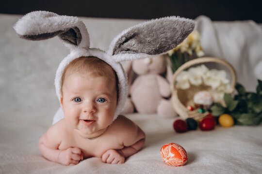 Cute little baby wearing bunny ears for Easter. Near Easter eggs. looks into the camera and smiles.
