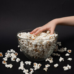 a child's hand on a black background takes popcorn from a bowl
