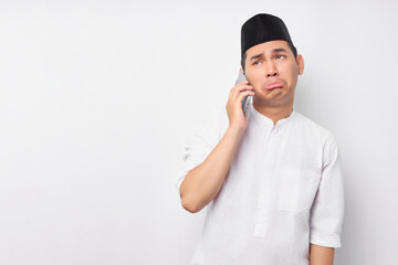 Portrait of sadness young Asian Muslim man in Arabic clothes talking on mobile phone with open mouth when receiving bad news isolated on white background. People religious Islamic lifestyle concept