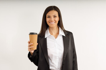 Portrait of happy pretty young woman in business suit holding paper cup of coffee in her hands on isolated white background. Studio shot of attractive brunette girl with snow-white smile.