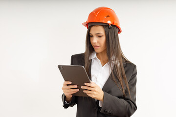 Portrait of young woman with tablet in her hands, dressed in business clothes on isolated white background. Studio shot of attractive happy brunette girl in orange construction helmet on her head.