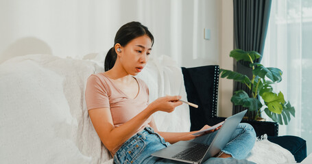 Asia businesswoman using laptop talk to colleagues about plan in video call while working from house at living room. Remotely at workplace, social distancing, quarantine for corona virus prevention.