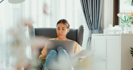 Young asia female girl or university student sit on sofa chair with computer laptop wear earphone...