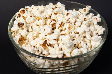 Glass and transparent bowl of fried popcorn on black background.