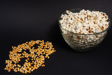 A bowl of fried popcorn and corn kernels on a black background