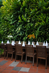 Decoration and set up of the dining table with nature green leaves and flower background. Wooden table, wooden chair, weaving mat table, weaving mat chair