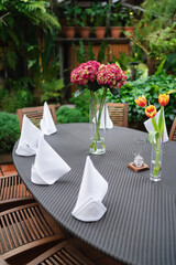 Decoration and set up of the dining table with nature green leaves and flower background. Wooden table, wooden chair, weaving mat table, weaving mat chair