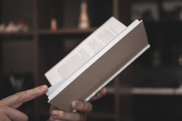 men's hands are holding an open book in a white cover on dark background.