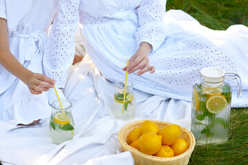 close up hands of mother and daughter drink refresh lemonade picnic on green grass in summer