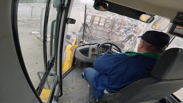 Man driving forward and backward a front loader while pushing, scooping, and dumping trash at a waste transfer station, inside the cabin view.