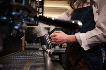 Close up of a barista preparing milk for coffee on a espresso machine in coffee shop. - obrazy, fototapety, plakaty