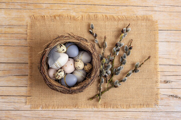Easter eggs in nest on the sackcloth with willow twigs. Easter festive background. Top view, flat...