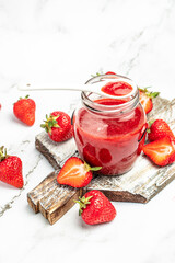 Strawberry jam in the glass jar with a spoon at white table. vertical image. top view