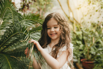 Little girl in the botanical garden. a girl in a white dress laughs near palm leaves.