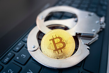 golden bitcoin on the background of handcuffs and a black laptop keyboard. Prohibition of the sale...
