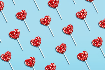 Lollipops in heart shape on blue background. Top view photo. Red and white sweet candies on stick. Minimal style
