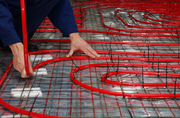 Worker is installing a red pipe for underfloor heating