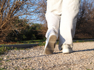 Low view of female legs in trendy high platform sneakers walking on a gray gravel path.