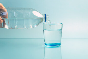Pouring water from bottle into glass blue background
