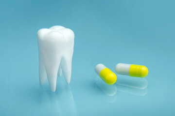 Close up view of yellow white pills and tooth model on blue background. painkillers. remedy for toothache.
