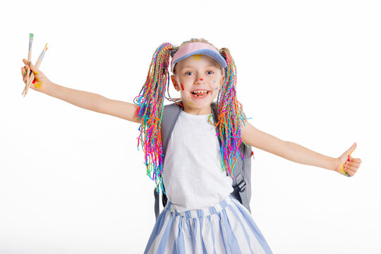 Curious preschooler kid girl stands on white background looking at camera wearing stylish clothes holds backpack and colorful painting braids ready to go to school after holidays.