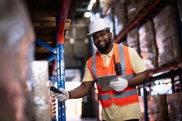 African American male warehouse worker scanning package with barcode scanner to count inventory balance in online system, holding tablet in hand for checking real time update in storage warehouse.