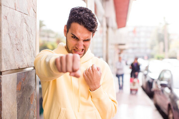 young hispanic man looking confident, angry, strong and aggressive, with fists ready to fight in boxing position