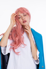 Barbie woman in pink wig touching her face with arms posing for camera wearing white t-shirt and blue jacket while shooting process.