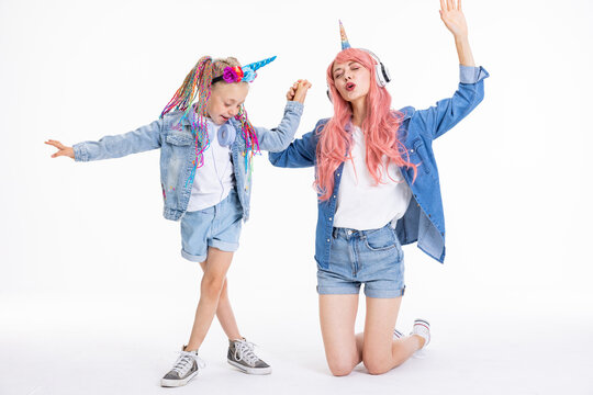 Pretty mother with cute preschooler daughter holding with hands dancing singing while shooting process wearing pink wig unicor headband and denim costume.