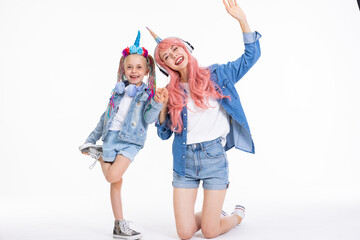 Happy adorable mother with pink wig and unicorn headband hugging preschooler daughter with braids...