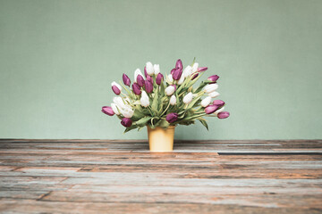 Bouquet of tulips in a yellow bucket in front of a green wall on wooden floor