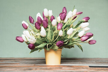 Bouquet of tulips in a yellow bucket in front of a green wall on wooden floor