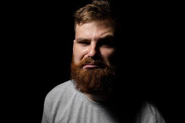 Obraz premium Close-up portrait of a handsome a brunette brutal bearded man in a grey t-shirt. Stylish and handsome man with a beard.