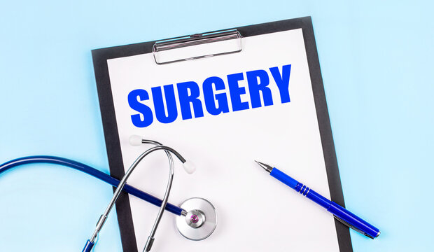 On a blue background, a stethoscope, a pen and a tablet with paper and the text SURGERY. Medical concept