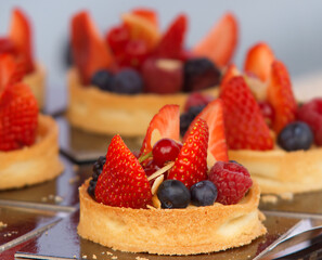 Fruit tarts embellished with raspberries, strawberries, blueberries and currant balls at farmers street food market in Prague. Closeup, no people, no AI.