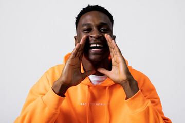 Stylish african american man guy in orange hoodie screaming yelling furious guy man over grey background in studio isolated.