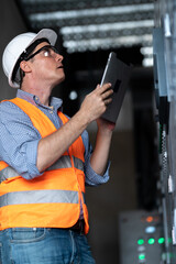 Professional industrial electrician in safety work wear checking power consumption on tablet computer.