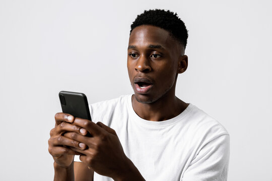 Portrait Close Up Shot Of African American Black Guy Holding New Modern Laste Series Cellphone Smartphone In Hands Observing Photos Receiving Bad News Emotional Guy Stunned Terrified.