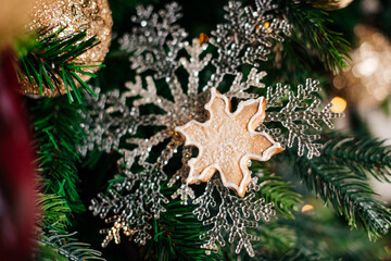 A sparkling Christmas ornament shaped like a snowflake hanging on a decorated tree.