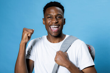 Cheerful happy ready to school university handsome african american man over blue background in studio isolated smiling wearing white t-shirt and backpack. Back to school university.