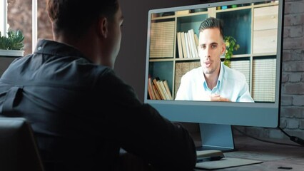 Concentrated skilled millennial caucasian businessman in glasses wearing headphones with mic, taking part in online web camera negotiations meeting using computer app, distant communication concept.
